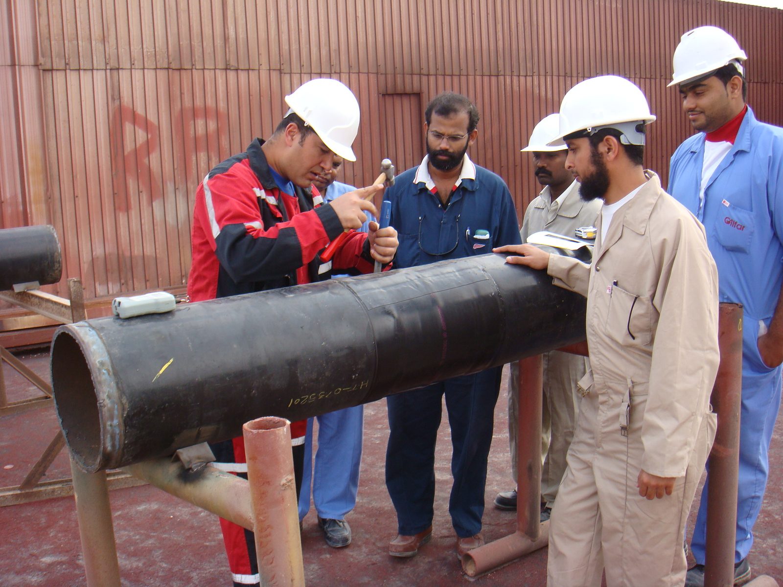 Ehab Abutahoun demonstrating a coating adhesion test on a coated pipe to a group of technicians