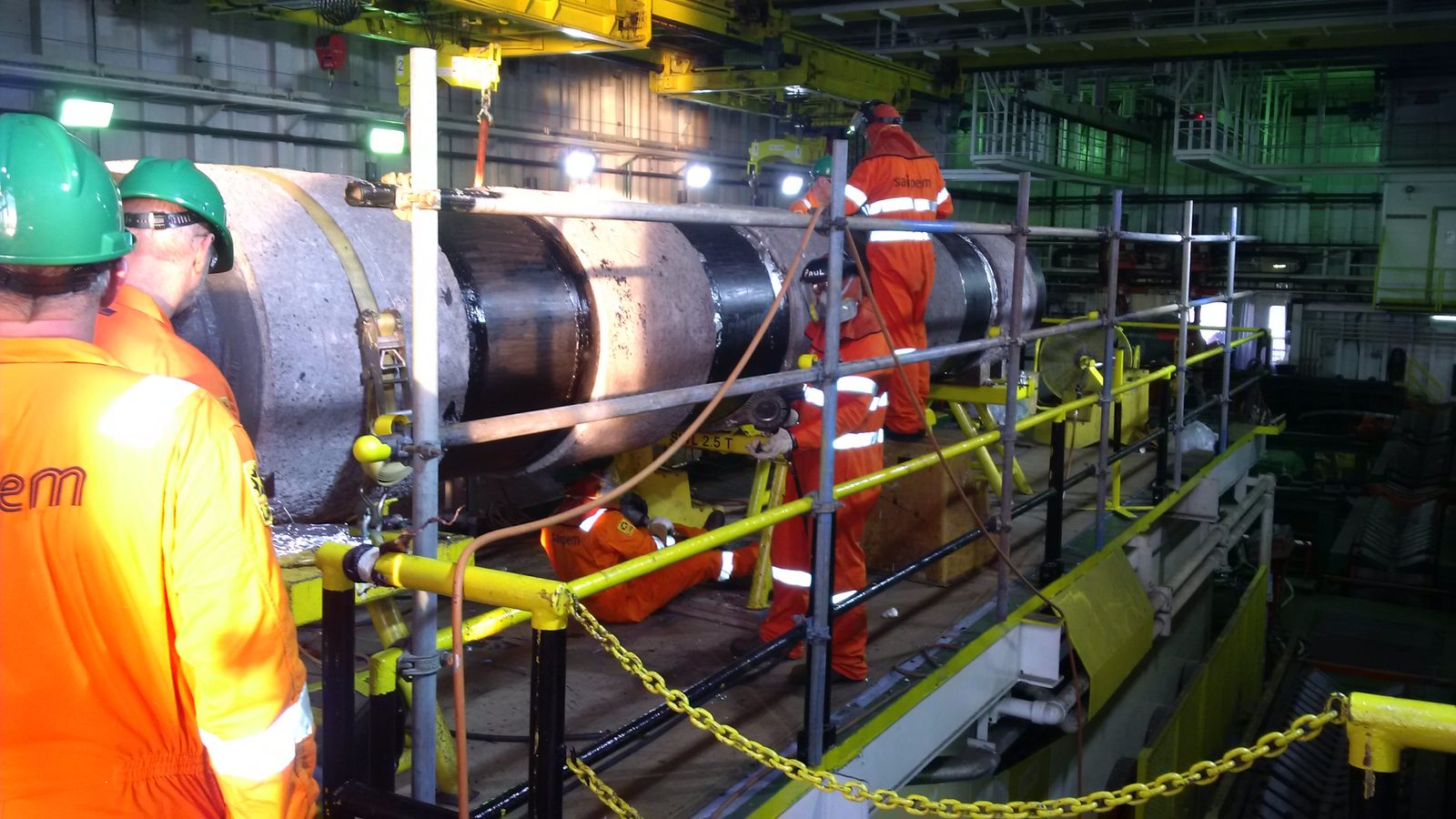 Technicians applying field joint coating to a concrete-weight-coated pipeline in an offshore firing line