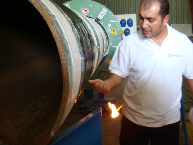 Ehab Abutahoun demonstrating heat-shrink sleeve application with a torch on a pipe joint