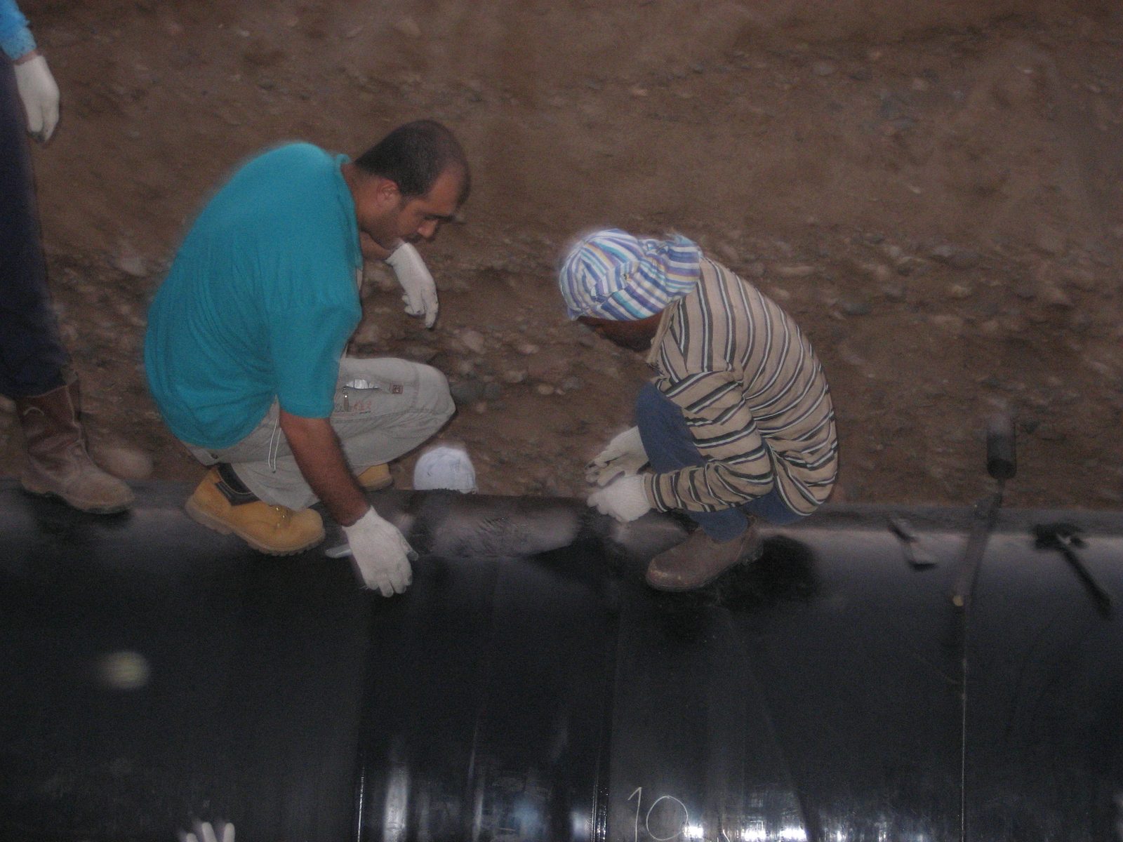 Two technicians applying coating repair material to a pipeline in a trench